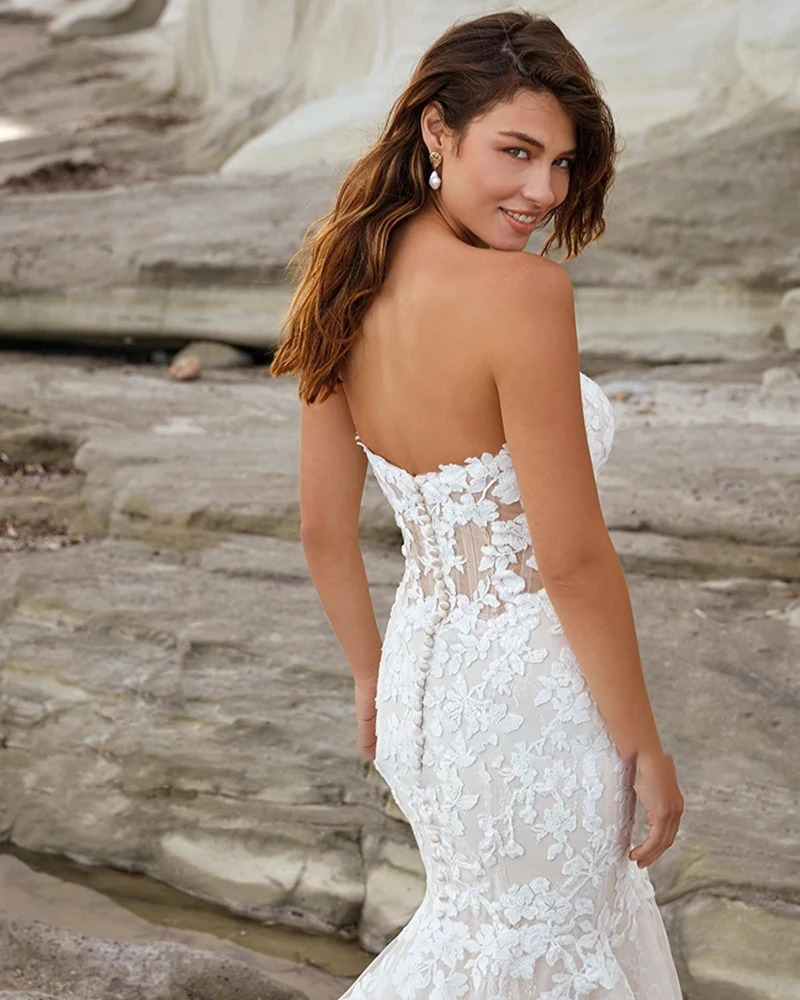 Rear view of a luxury backless mermaid bridal gown showcasing a low V-cut back, illusion mesh profiling, and an expansive flared tulle train layout.
