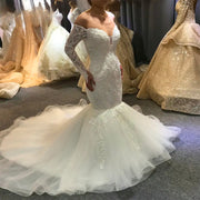 Side profile of an elegant mermaid wedding dress featuring off-the-shoulder lace long sleeves and a dramatic flared ruffled train.