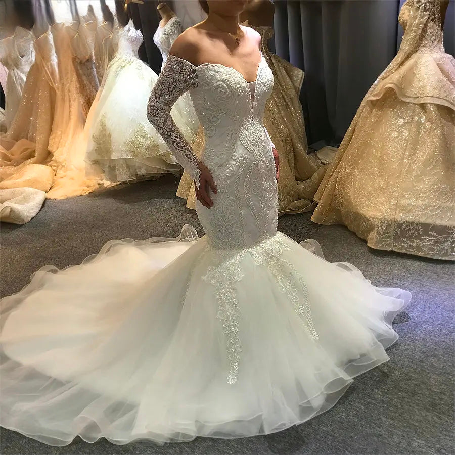 Side profile of an elegant mermaid wedding dress featuring off-the-shoulder lace long sleeves and a dramatic flared ruffled train.