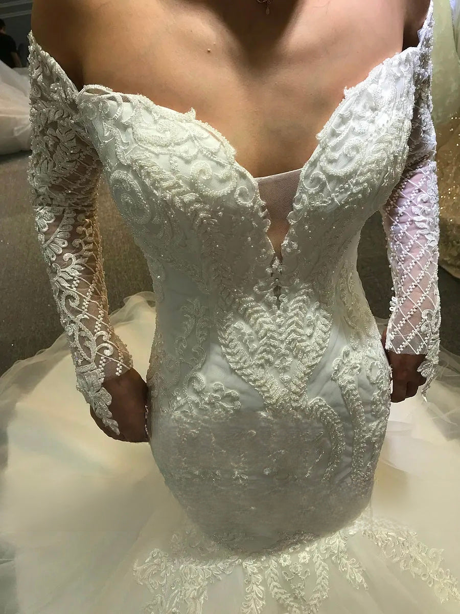 Close-up of the sweetheart bodice and long lace sleeves of a mermaid wedding dress, detailing the luxury beadwork and illusion plunge.