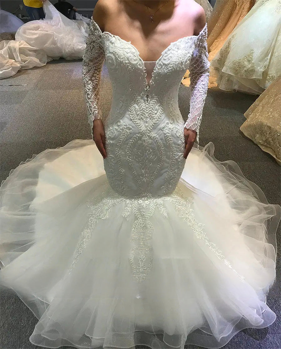 Front shot of a fitted mermaid wedding gown showing the ornate lace embroidery and the transition to a ruffled tulle skirt.