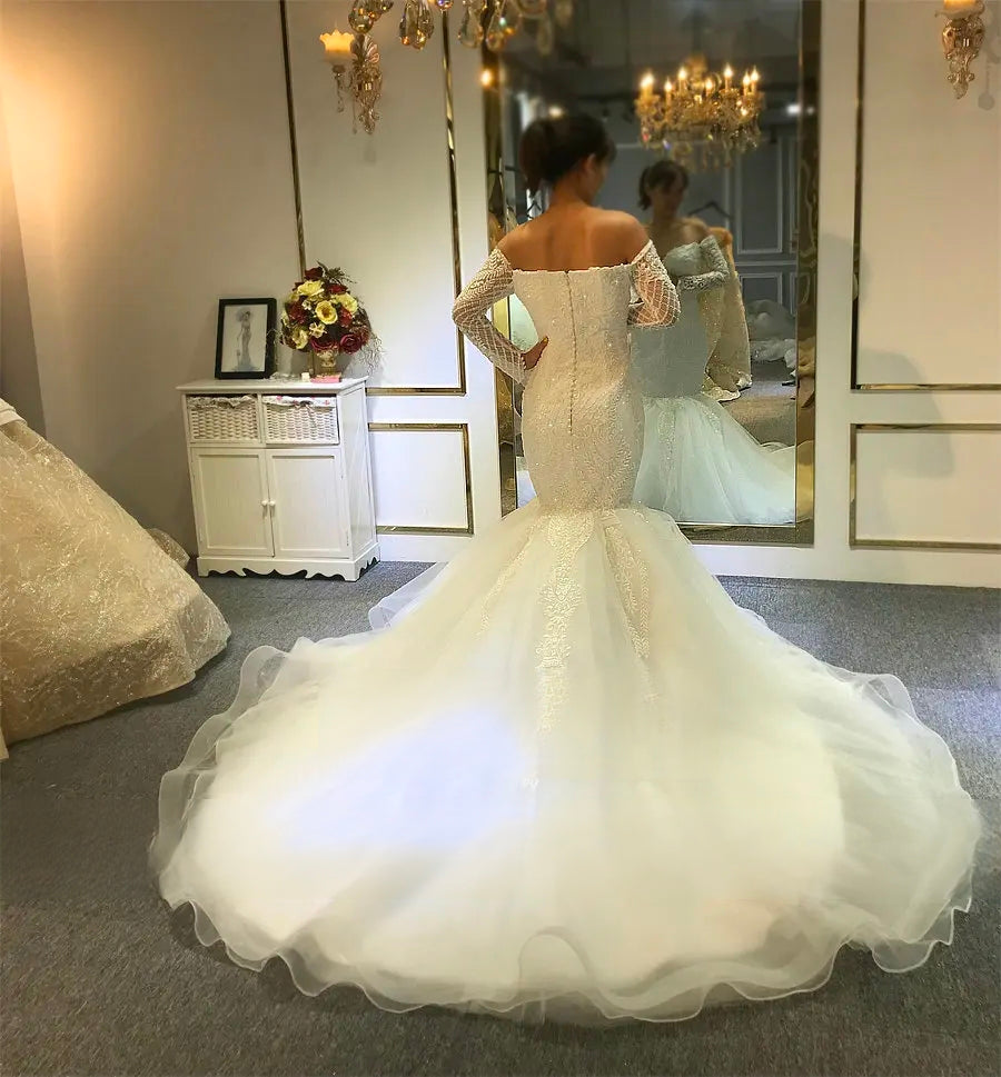 Full back view of an off-the-shoulder mermaid bridal gown with a sweeping circular ruffled train in a luxury boutique setting.