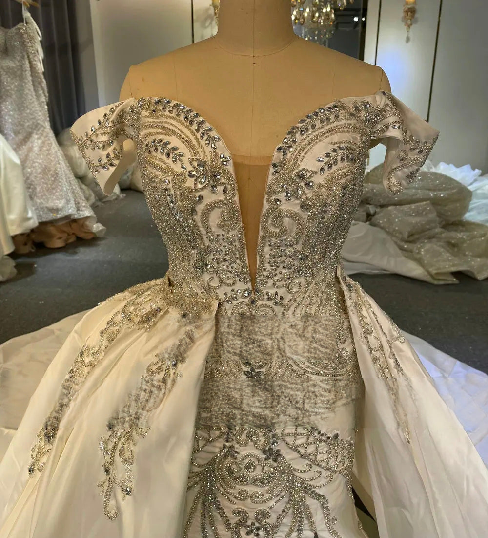 Close-up detail of a bridal gown's beaded bodice, featuring a deep sweetheart neckline with illusion mesh and sparkling sequin embroidery on luxury off-the-shoulder Mikado satin.