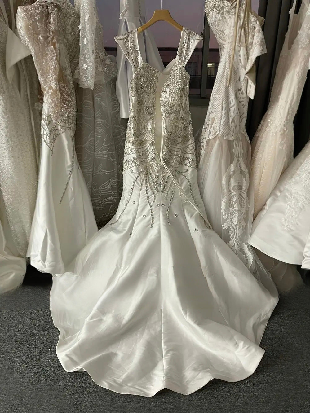 Back view of a trumpet wedding gown in Mikado satin, displaying the intricate crystal beadwork along the hips and the elegant floor-length mermaid train hanging in a bridal boutique.