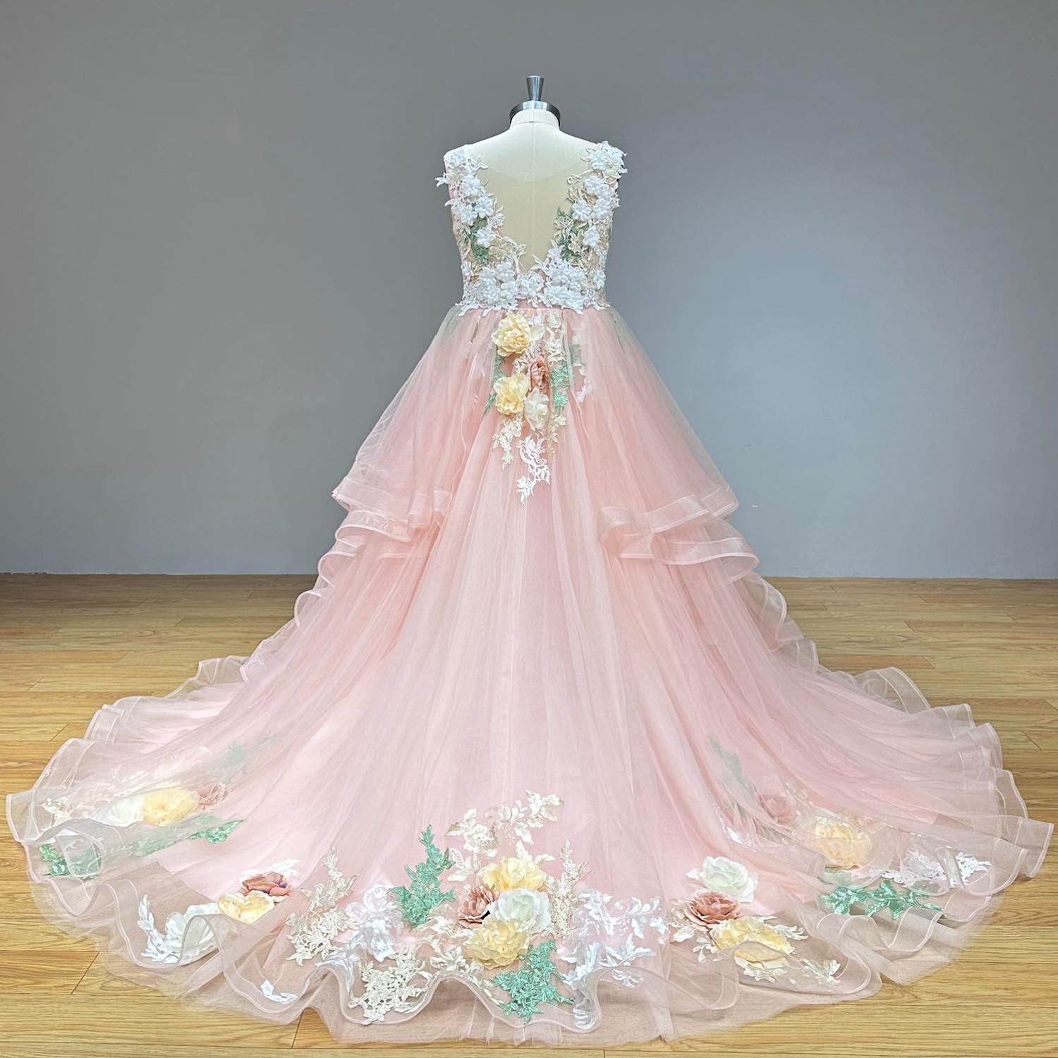 Complete studio back view of a blush pink princess wedding dress on a dress form, displaying the wide-sweeping tulle train adorned with a colorful border of embroidered vines and fabric flowers.