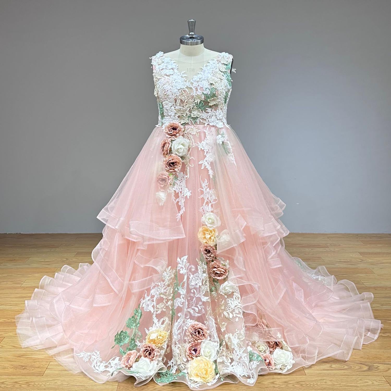Full front view of a non-traditional pastel pink wedding gown on a mannequin, highlighting the contrast between the white botanical lace bodice and the tiered pink horsehair trim skirt layers.