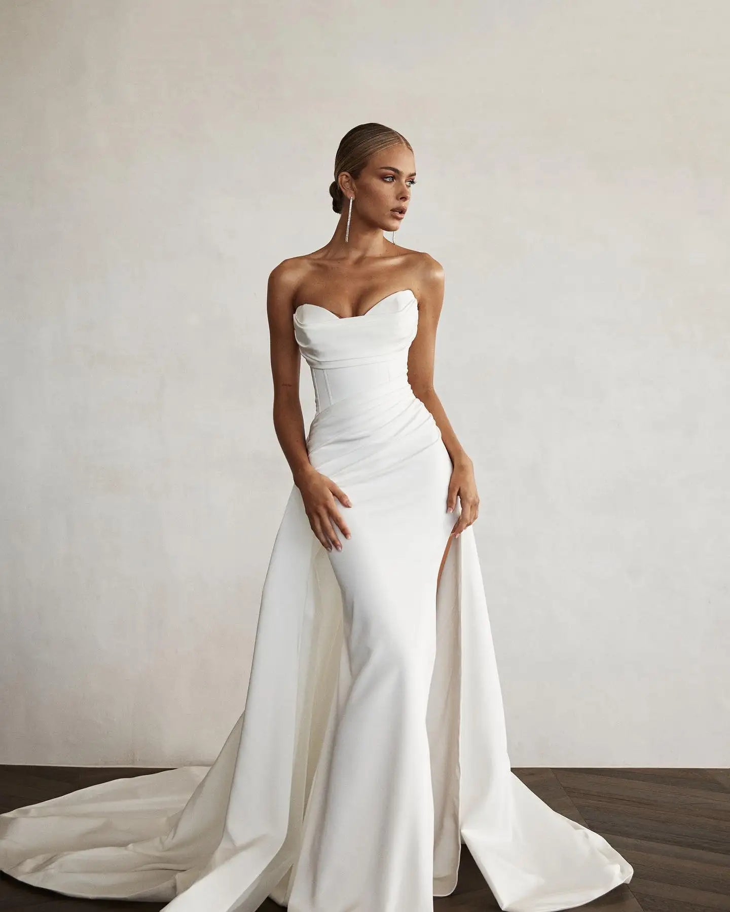 Front view of a modern mermaid bridal gown, showcasing a high front slit, a sweeping train, and a structured, elegant sweetheart neckline.