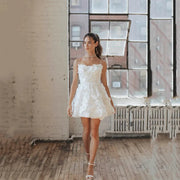Modern short A-line wedding dress featuring thin spaghetti straps, a fitted bodice covered in 3D textured floral appliques, and a flirty volumetric mini skirt.