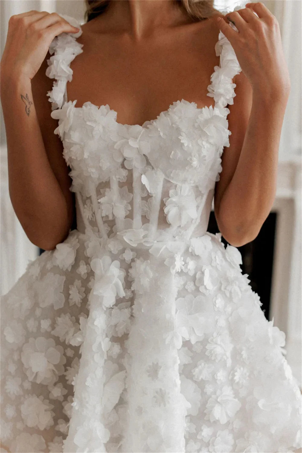 Detailed close-up of a short white bridal gown bodice, highlighting the dense layout of 3D lace flowers, supportive dual straps, and exposed boning on a sheer corset.