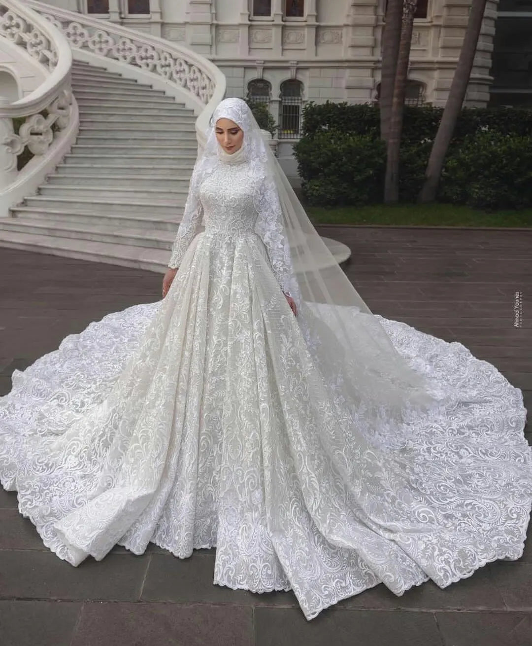A bride posing elegantly in a luxury long-sleeve A-line Muslim wedding dress with intricate lace detailing and a matching bridal hijab.