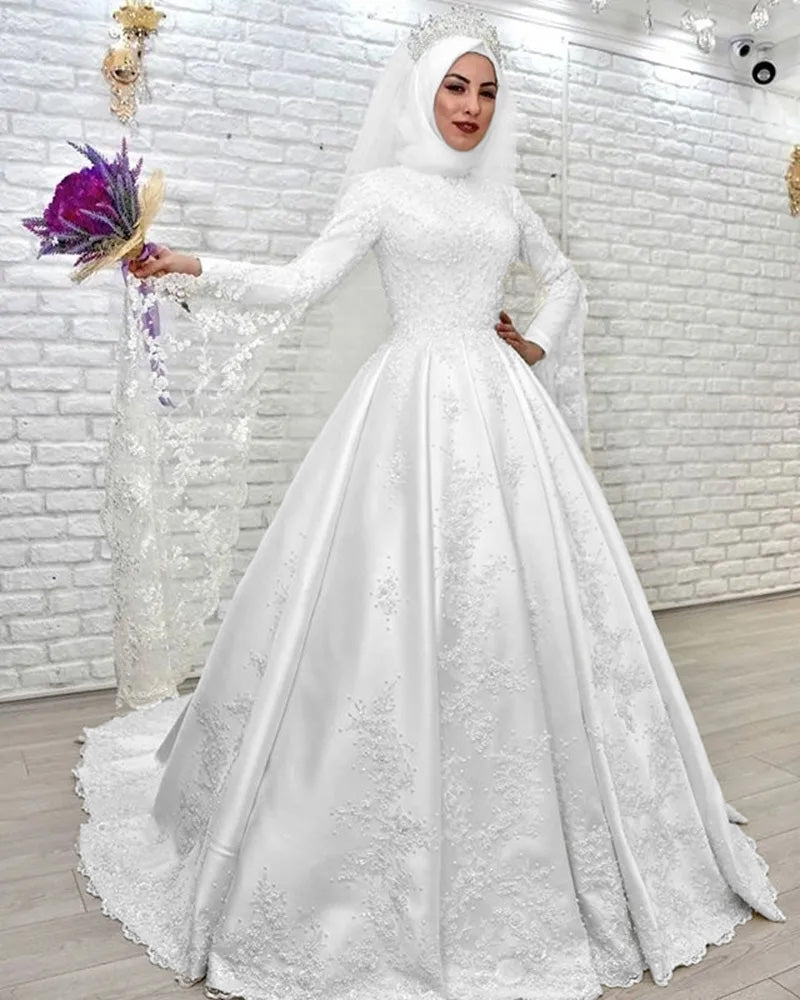 A full view of an elegant, modest Muslim wedding dress on a bride holding a bouquet, emphasizing the intricate lace and high-neck design.