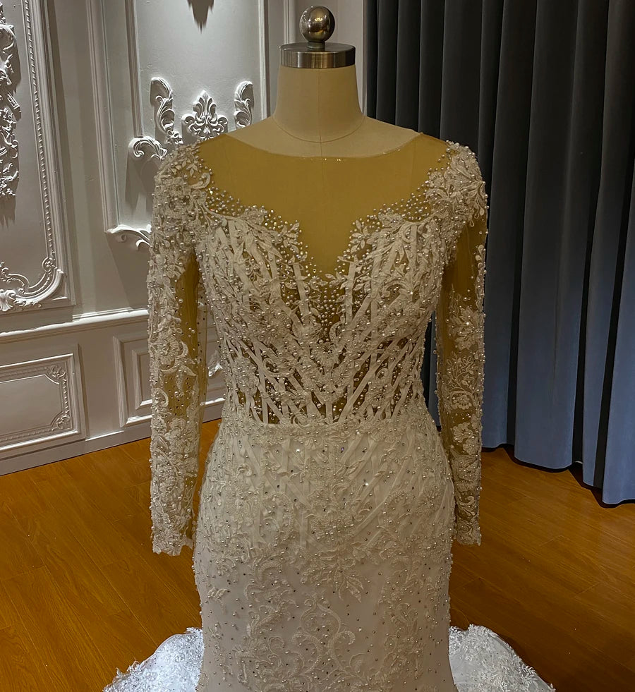 Close-up of the bodice and illusion neckline of a long-sleeved African mermaid wedding dress with pearl and crystal embellishments.