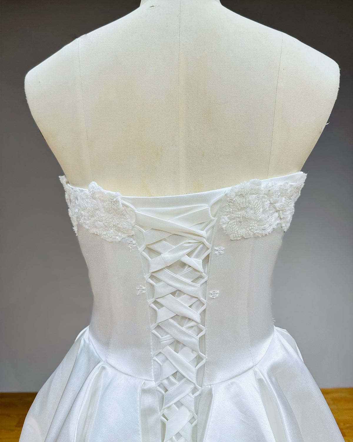 High-resolution macro shot of the adjustable satin ribbon lace-up back and intricate white pearl beadwork on the bodice of a couture wedding gown.