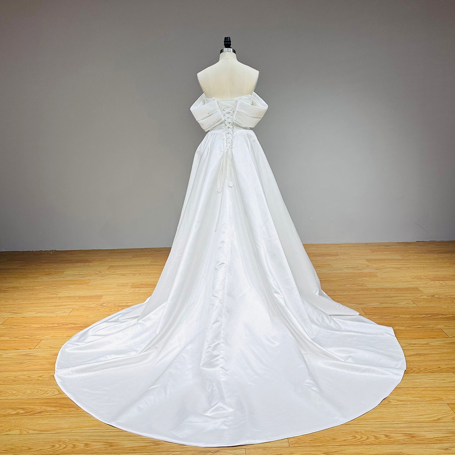 Full-length back view of a white satin wedding gown on a mannequin showcasing a classic lace-up corset back and a voluminous, sweeping satin train.