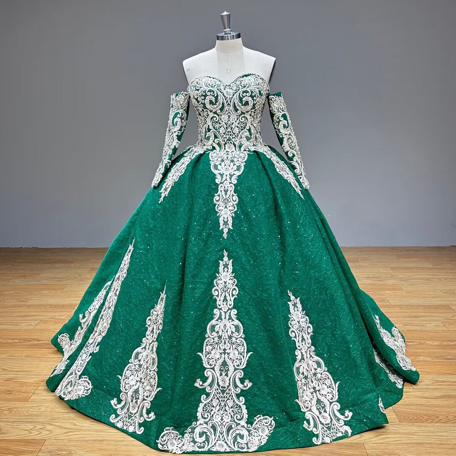 Studio product photography of the shining emerald green tulle ball gown on a mannequin, showcasing the strapless sweetheart bodice and detachable arm sleeves.