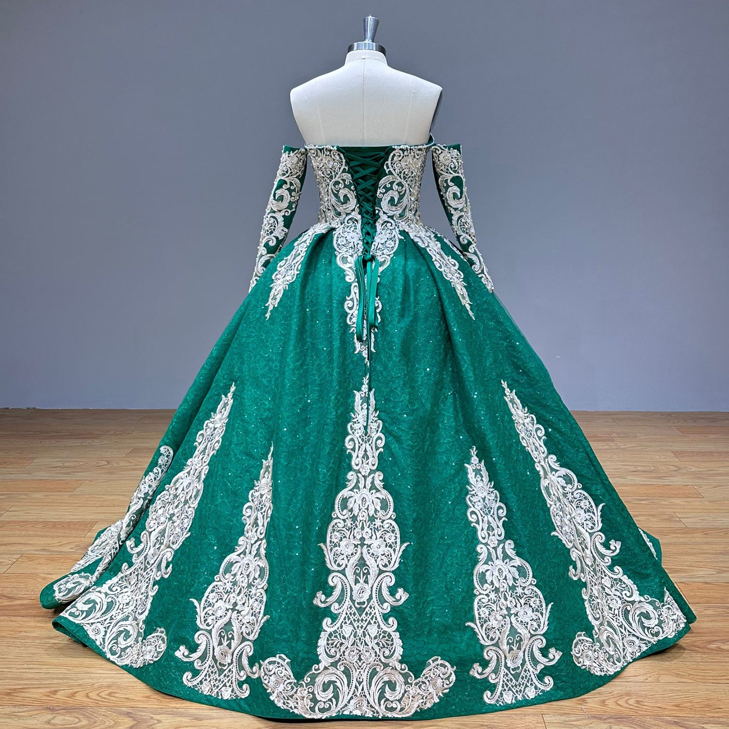 Full back view of the emerald green formal gown on a mannequin, emphasizing the adjustable ribbon corset closure and symmetrical silver embroidery trailing down the wide train.