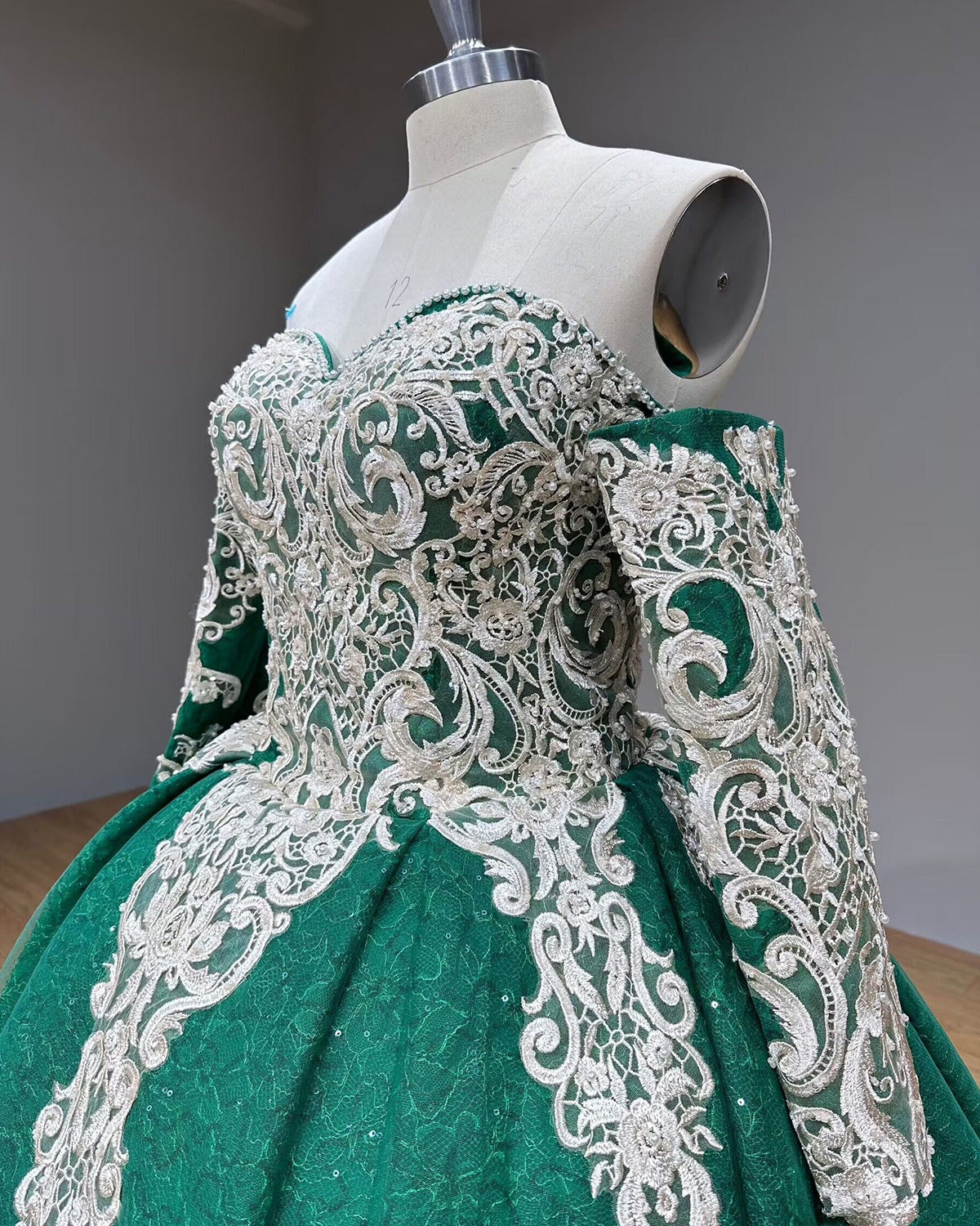 Three-quarter side angle close-up of the emerald green dress bodice, showcasing the textured silver lace patterns and matching detached sleeves on a studio mannequin.