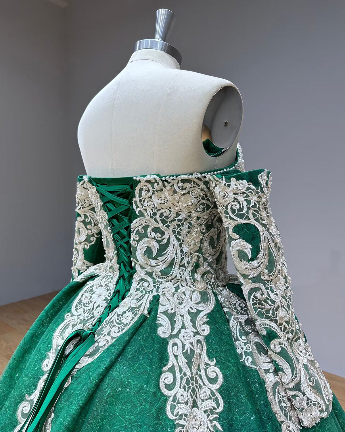 Angled close-up of the dress back showing the emerald green ribbon corset lacing system and scrolling silver lace appliques over glittering tulle.