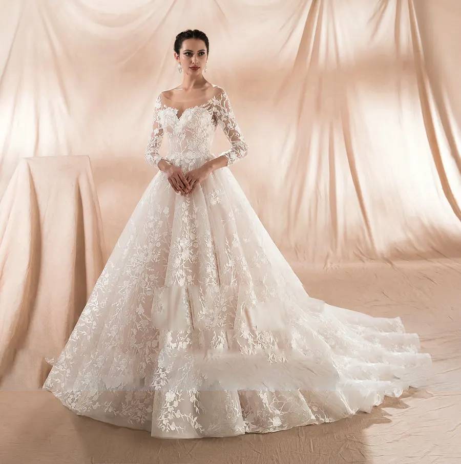 Full-length front view of an elegant champagne A-line wedding dress featuring long sleeves and intricate white floral lace overlays.