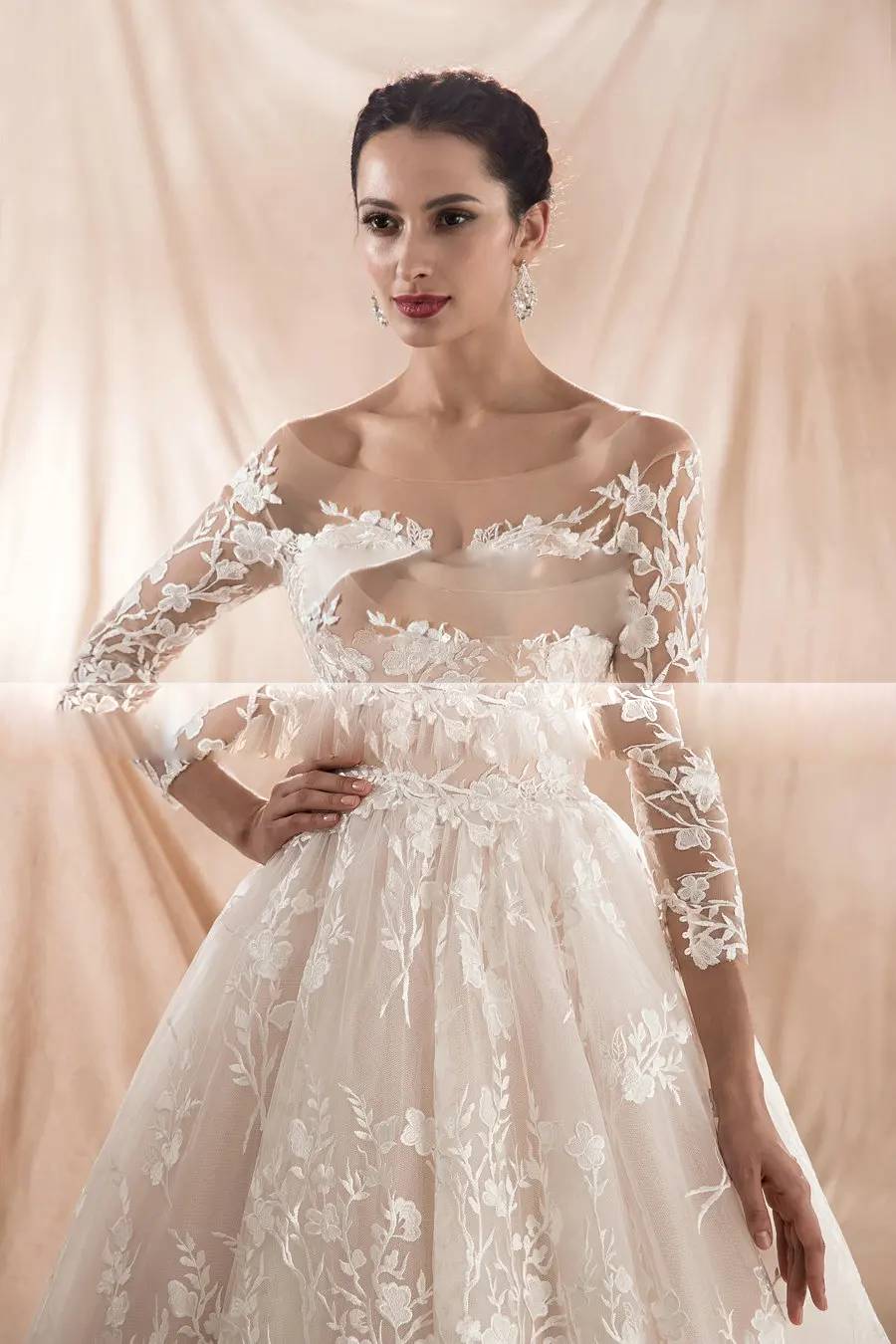Close-up detail of a champagne bridal gown bodice showcasing a sheer illusion neckline and delicate floral lace embroidery on the sleeves.