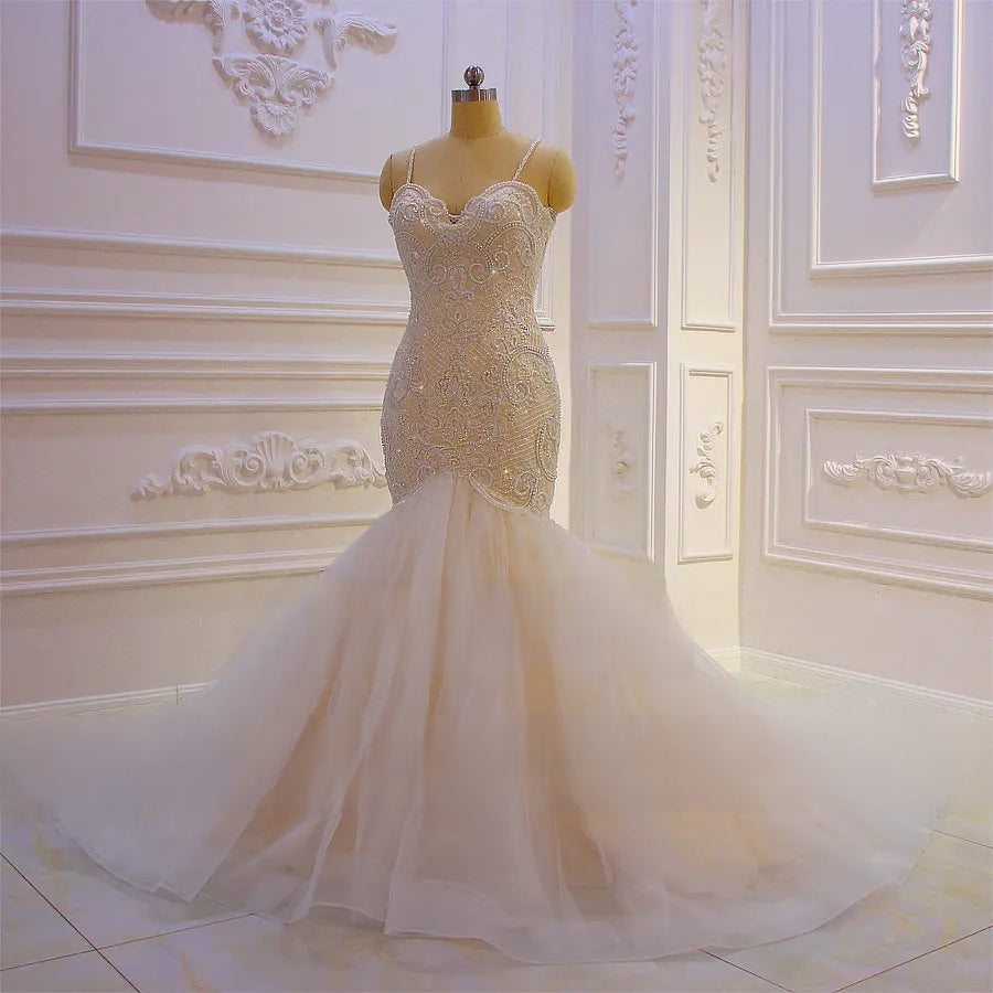 Elegant mermaid wedding gown featuring intricate beaded lace detailing and spaghetti straps, displayed on a mannequin in a showroom.