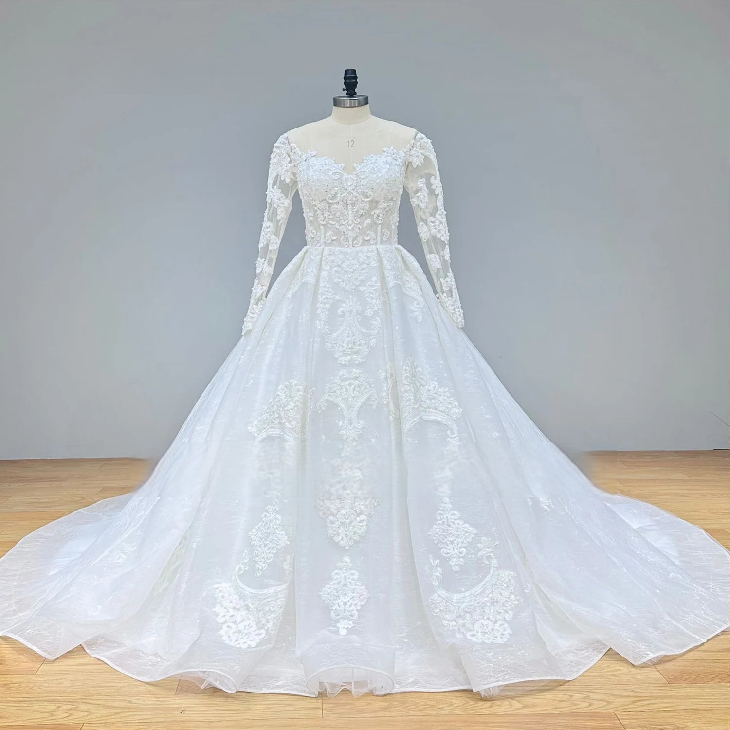 Full-length front display of an ivory O-neck long sleeve lace ball gown wedding dress on a mannequin, highlighting the ornate symmetrical lace appliques.