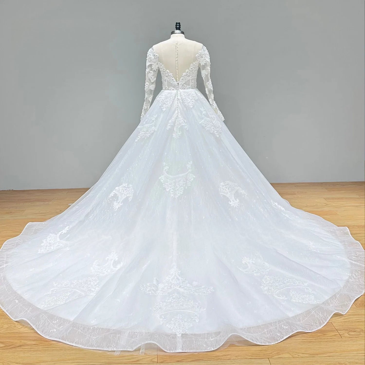 Rear view of the lace ball gown wedding dress on a mannequin, showcasing the sheer illusion V-back design and a dramatic, sweeping cathedral train.