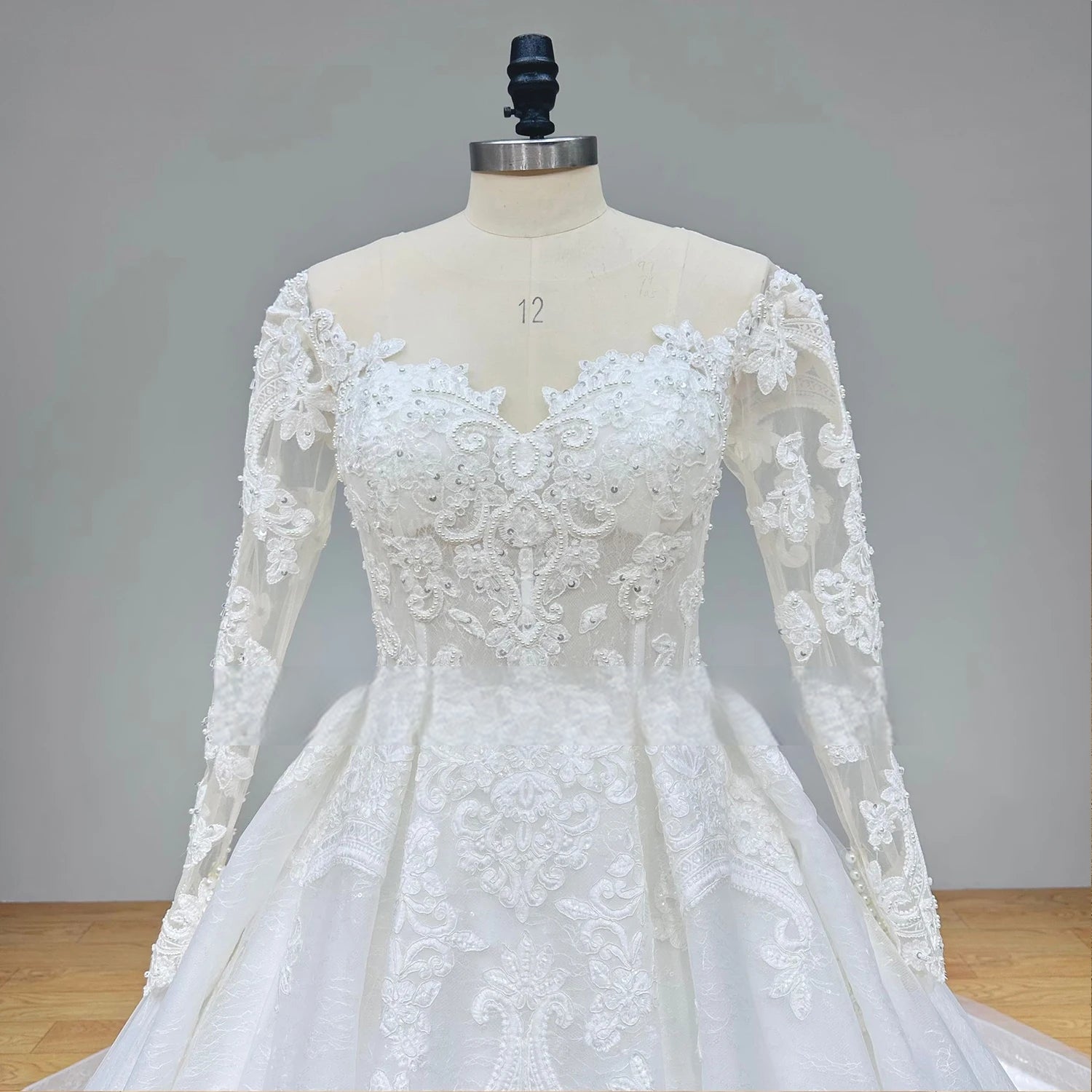 Close-up front view of the bridal bodice on a mannequin, detailing the sweetheart illusion neckline, sheer lace sleeves, and shimmering crystal beadwork.