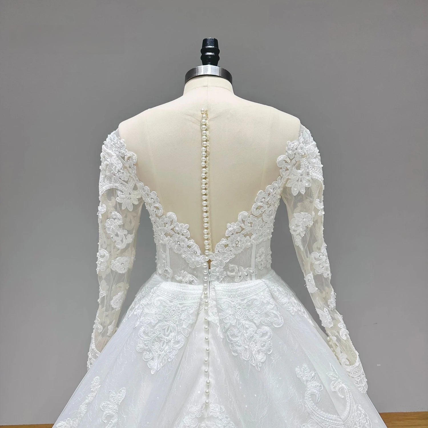 Detailed close-up of the back bodice of the bridal gown, highlighting the sheer illusion lace back secured with a classic row of elegant pearl buttons.