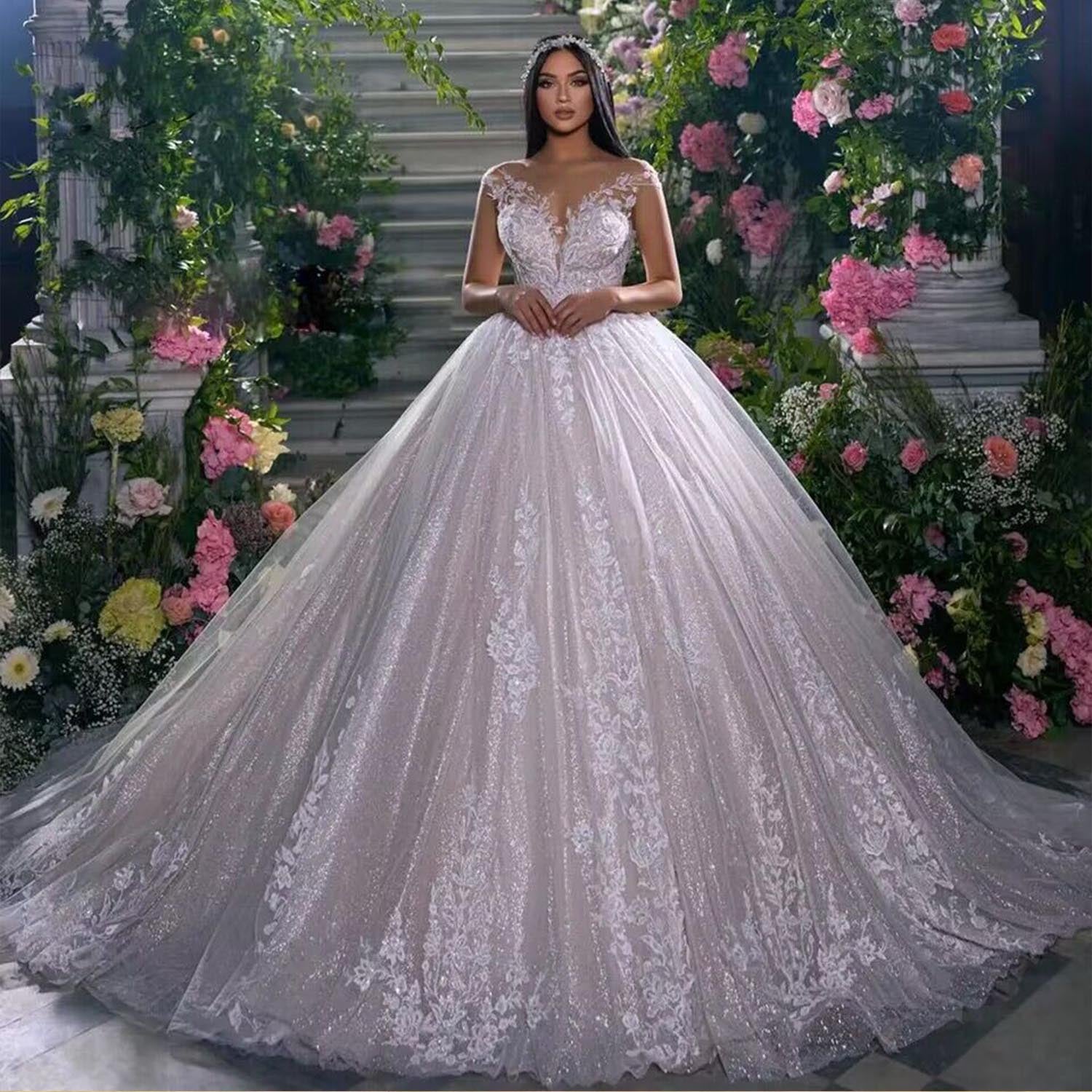 A beautiful bride in a lush floral setting wearing a new arrival off-shoulder ball gown wedding dress, featuring sparkling sequined tulle and delicate lace appliques.