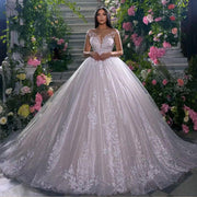 A beautiful bride in a lush floral setting wearing a new arrival off-shoulder ball gown wedding dress, featuring sparkling sequined tulle and delicate lace appliques.