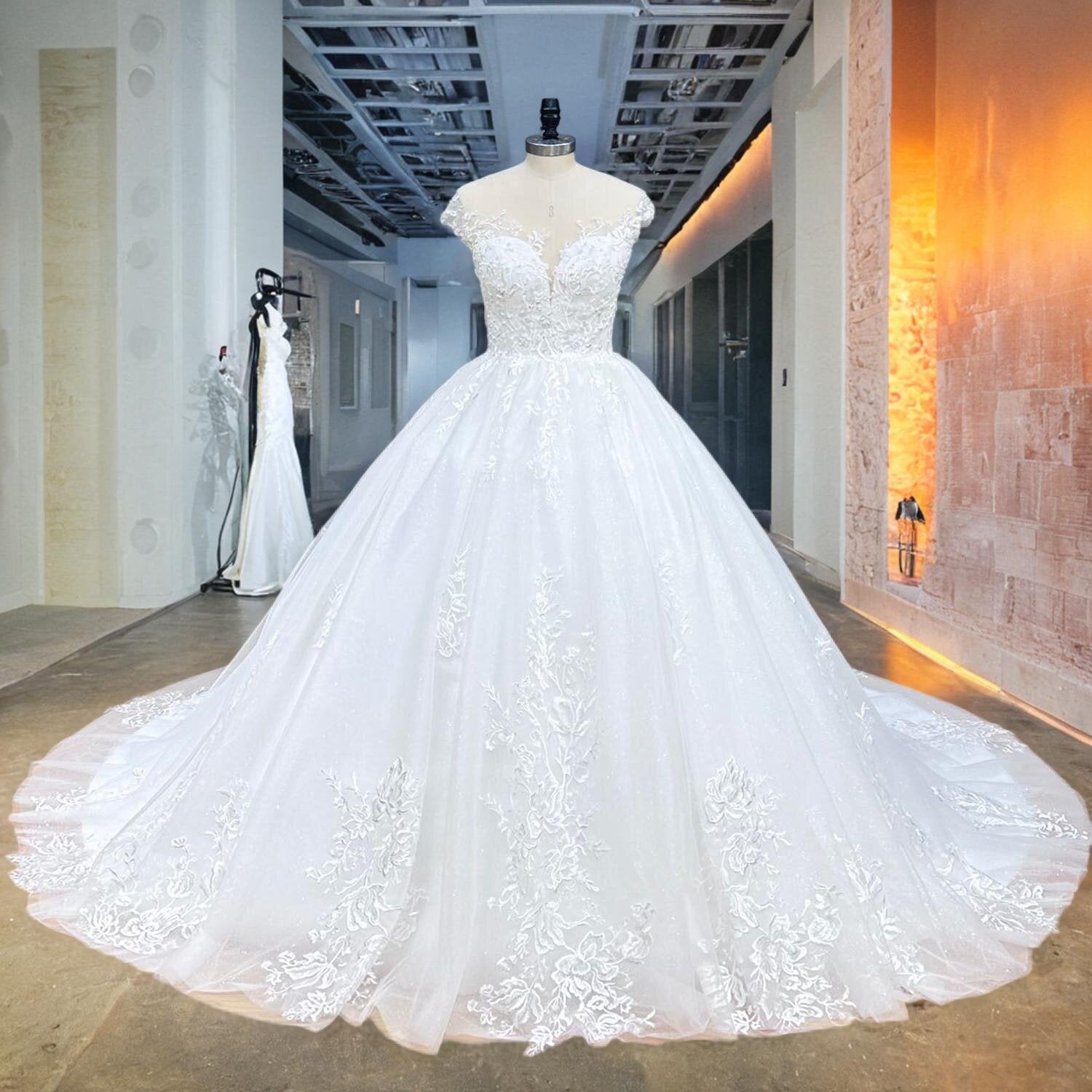 Full front view of a shimmering new arrival off-shoulder ball gown wedding dress on a mannequin, showcasing a sweetheart illusion neckline and sequined floral lace details in a studio hallway.