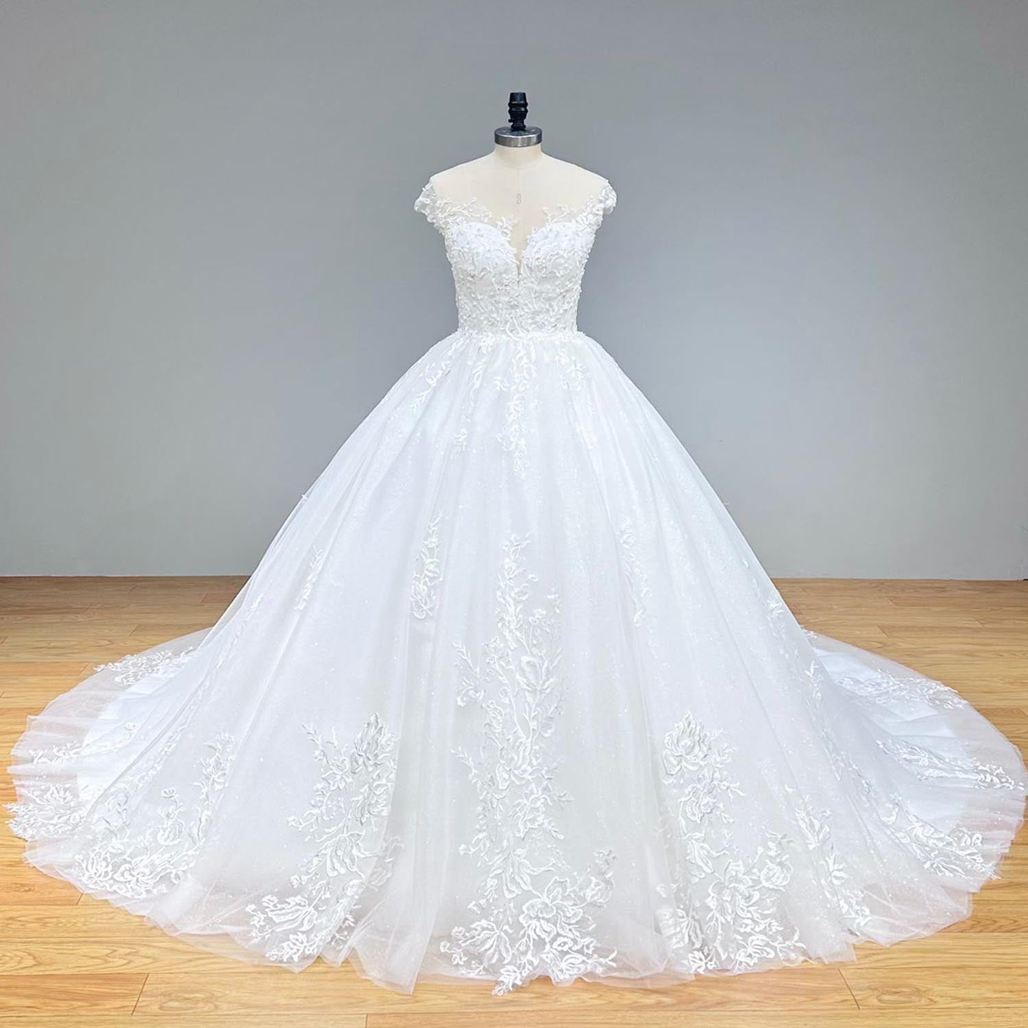 Classic front view of a romantic off-shoulder ball gown wedding dress on a mannequin, highlighting the voluminous sequined skirt and elegant cap sleeves against a grey backdrop.