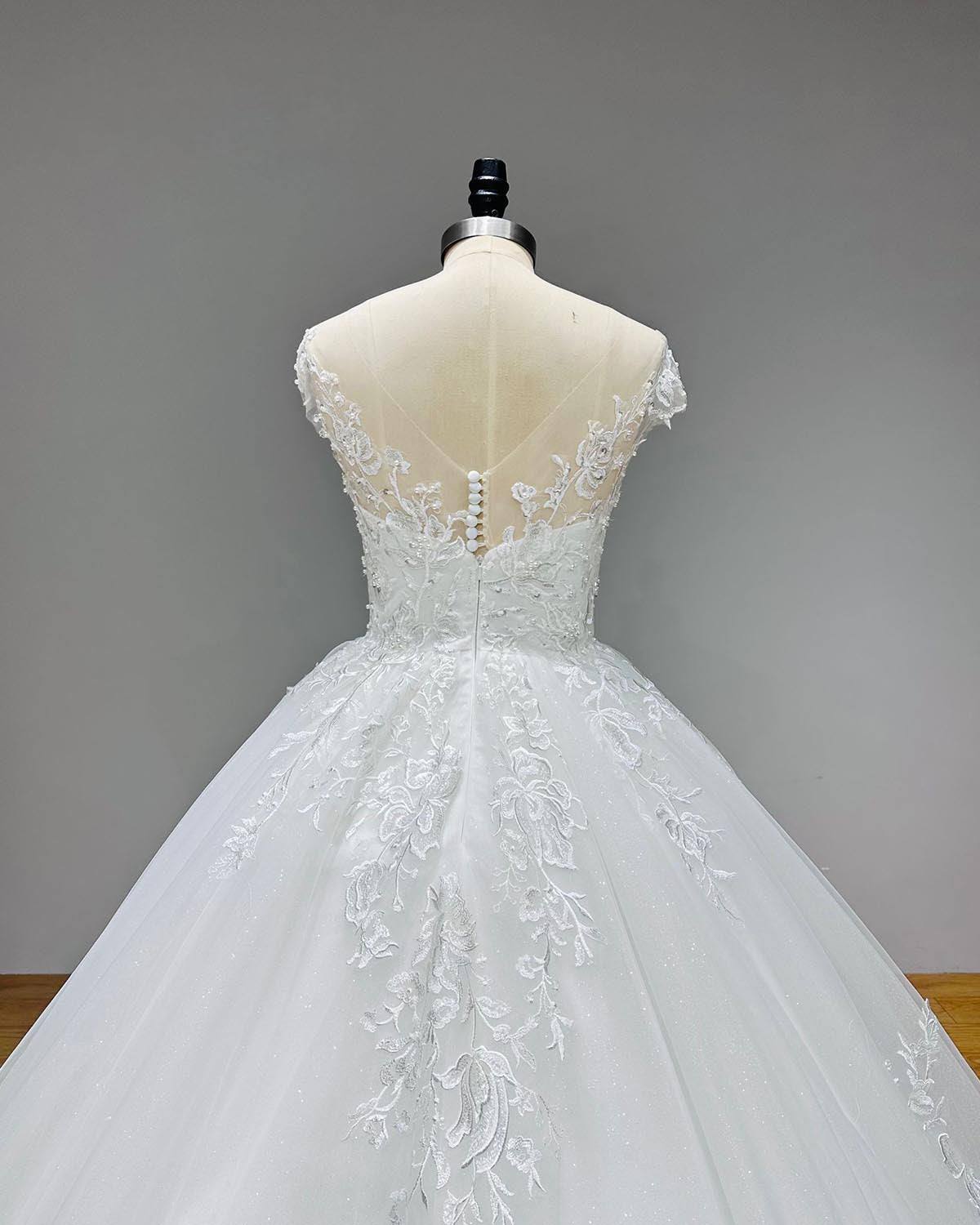 Close-up back bodice view of a backless illusion wedding dress, detailing the delicate pearl button closure, sheer mesh, and sequined lace appliques.