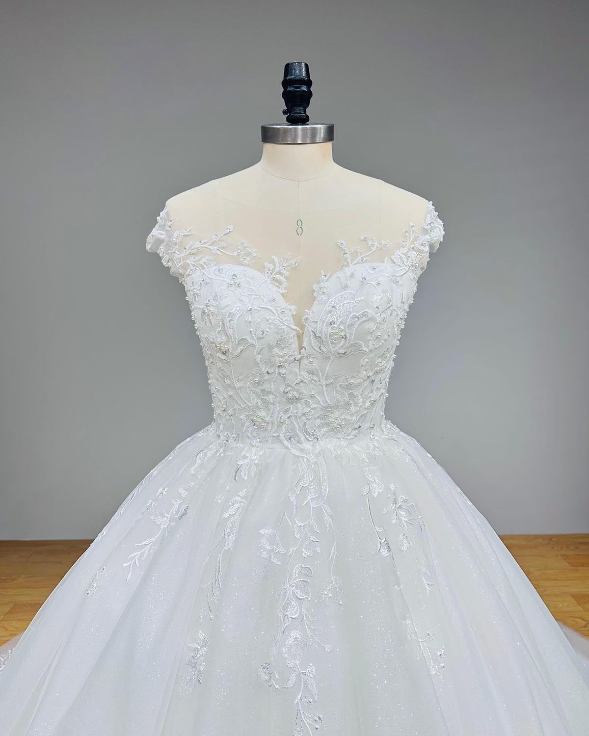 Close-up front bodice detail of a new arrival off-shoulder wedding gown on a mannequin, emphasizing the sheer plunging neckline, intricate beadwork, and sequined embroidery.