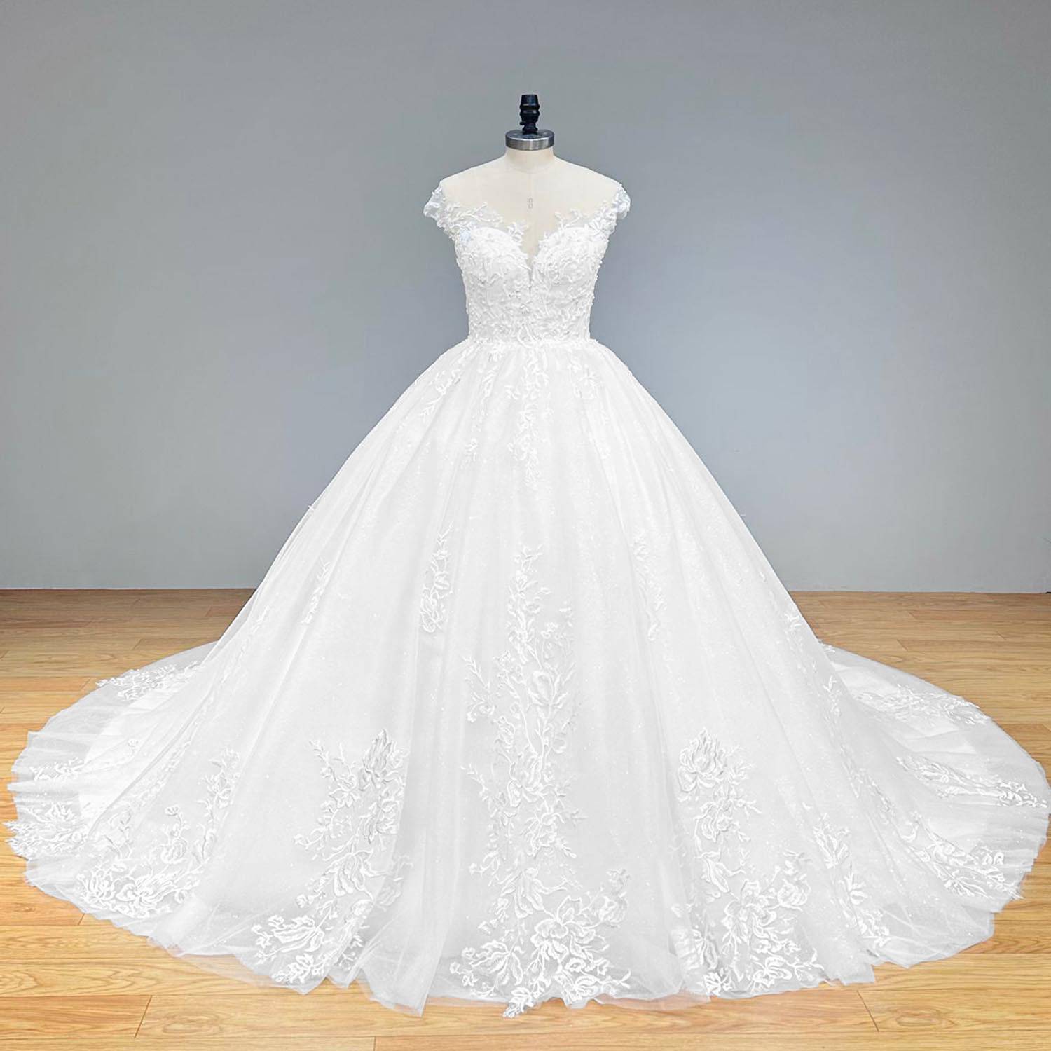 Elegant full front view of a bright, shimmering off-shoulder ball gown wedding dress on a mannequin, featuring a regal tulle skirt decorated with sequined floral appliques.