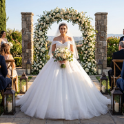 Bride posing outdoors in a luxury glitter short-sleeve ball gown wedding dress with a sweetheart neckline and elegant tassel back detail.