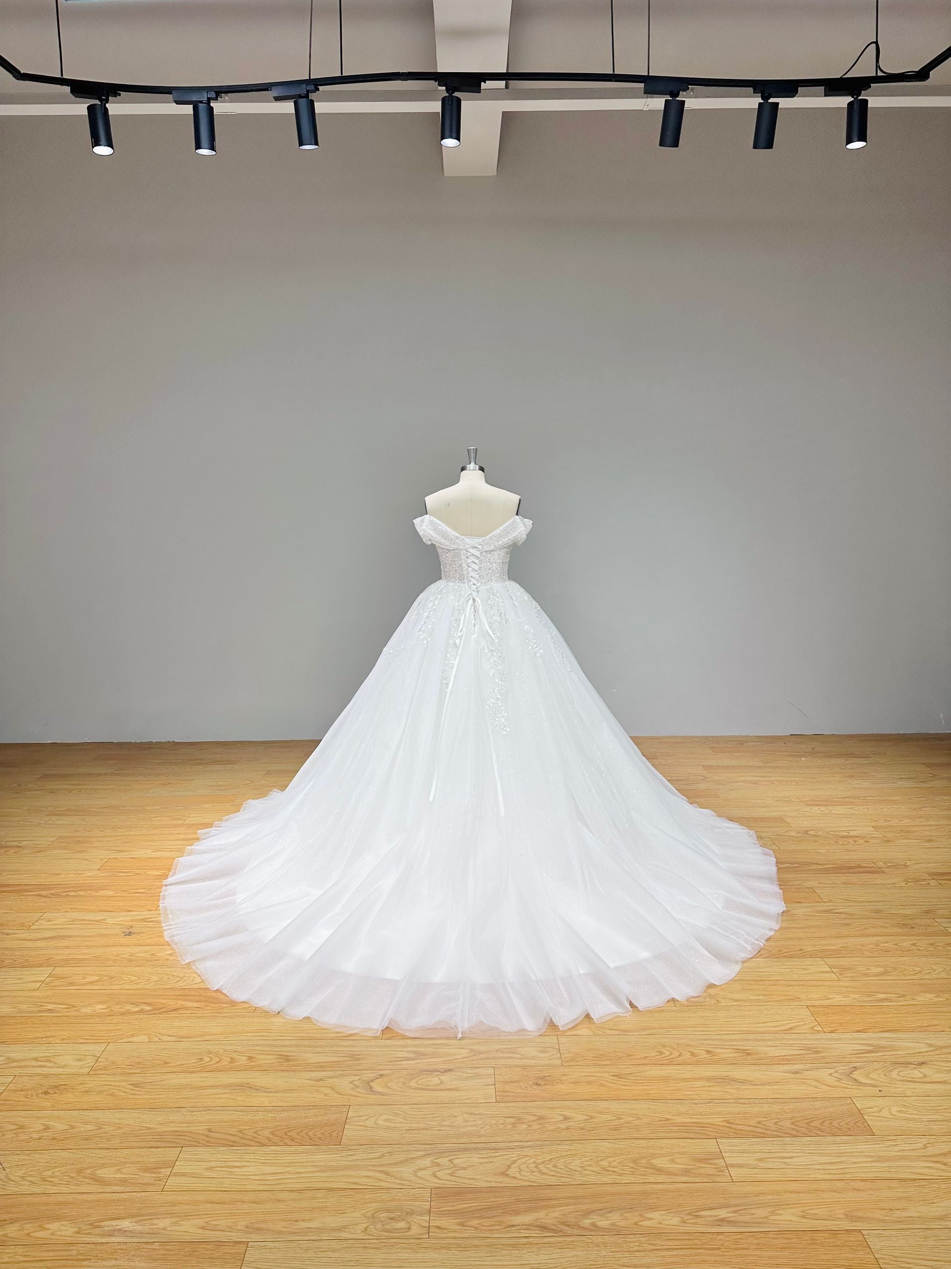 Detailed back view of an off shoulder ball gown bridal dress featuring a lace up back corset and pearl embellishments.