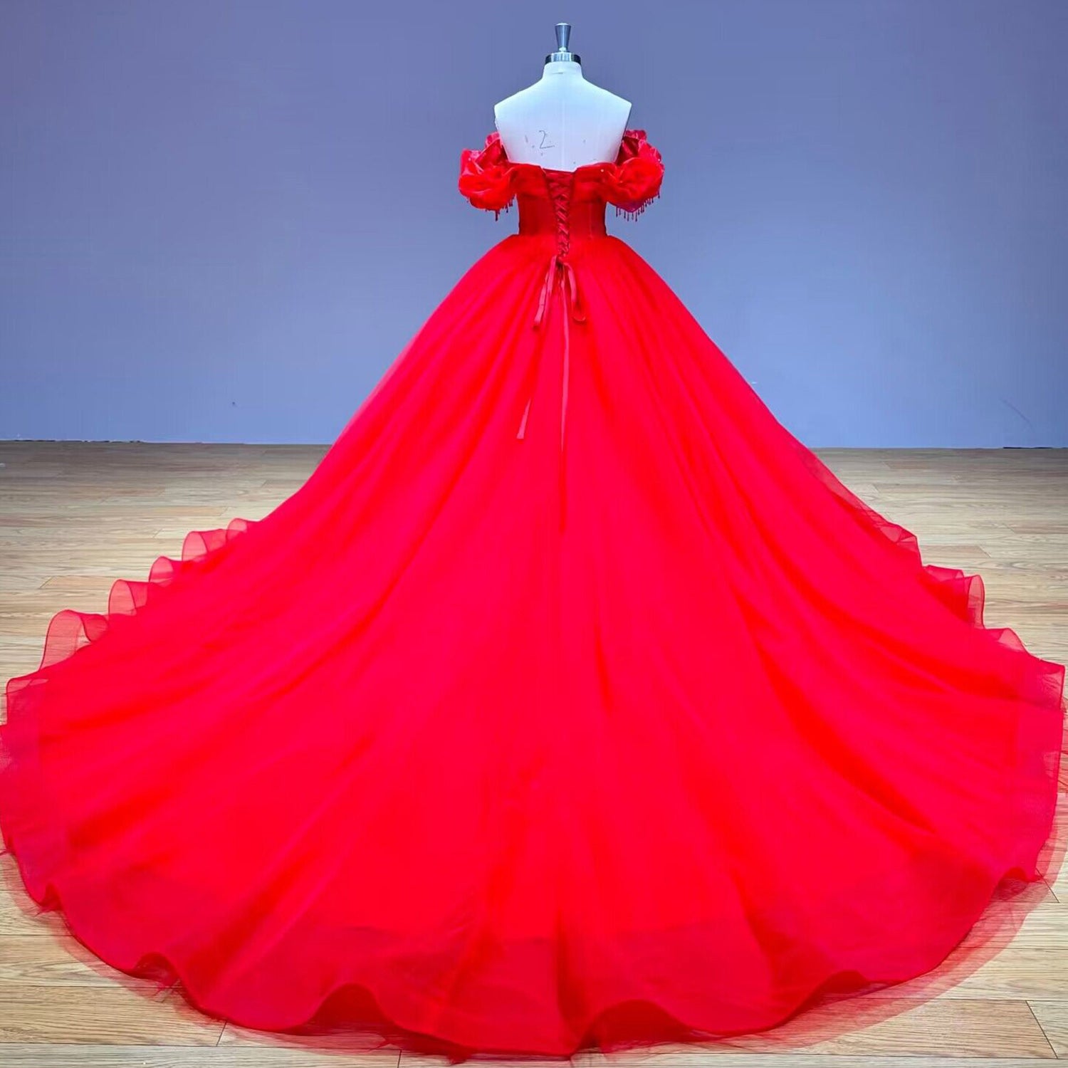 Full back view of the red tulle ball gown on a studio mannequin, highlighting the adjustable lace-up ribbon corset back and a massive sweeping train.