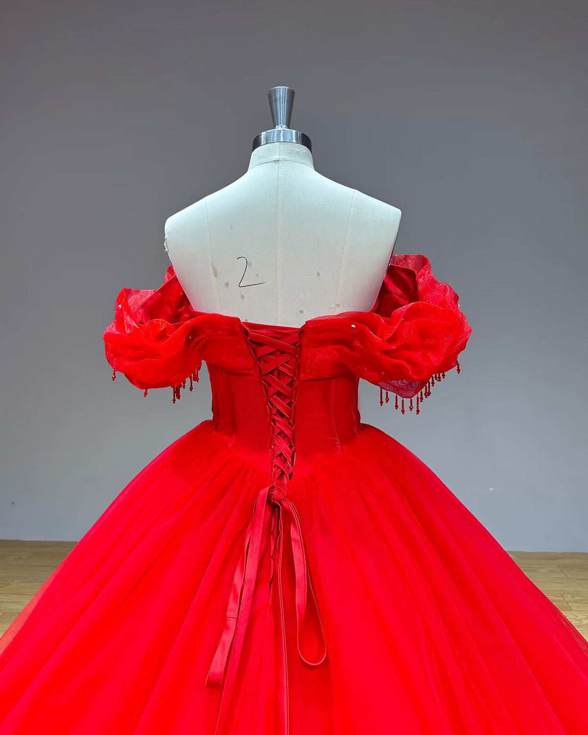 Close-up back view of the red wedding dress bodice focusing on the satin ribbon lace-up corset closure and delicate hanging bead fringe on the draped sleeves.
