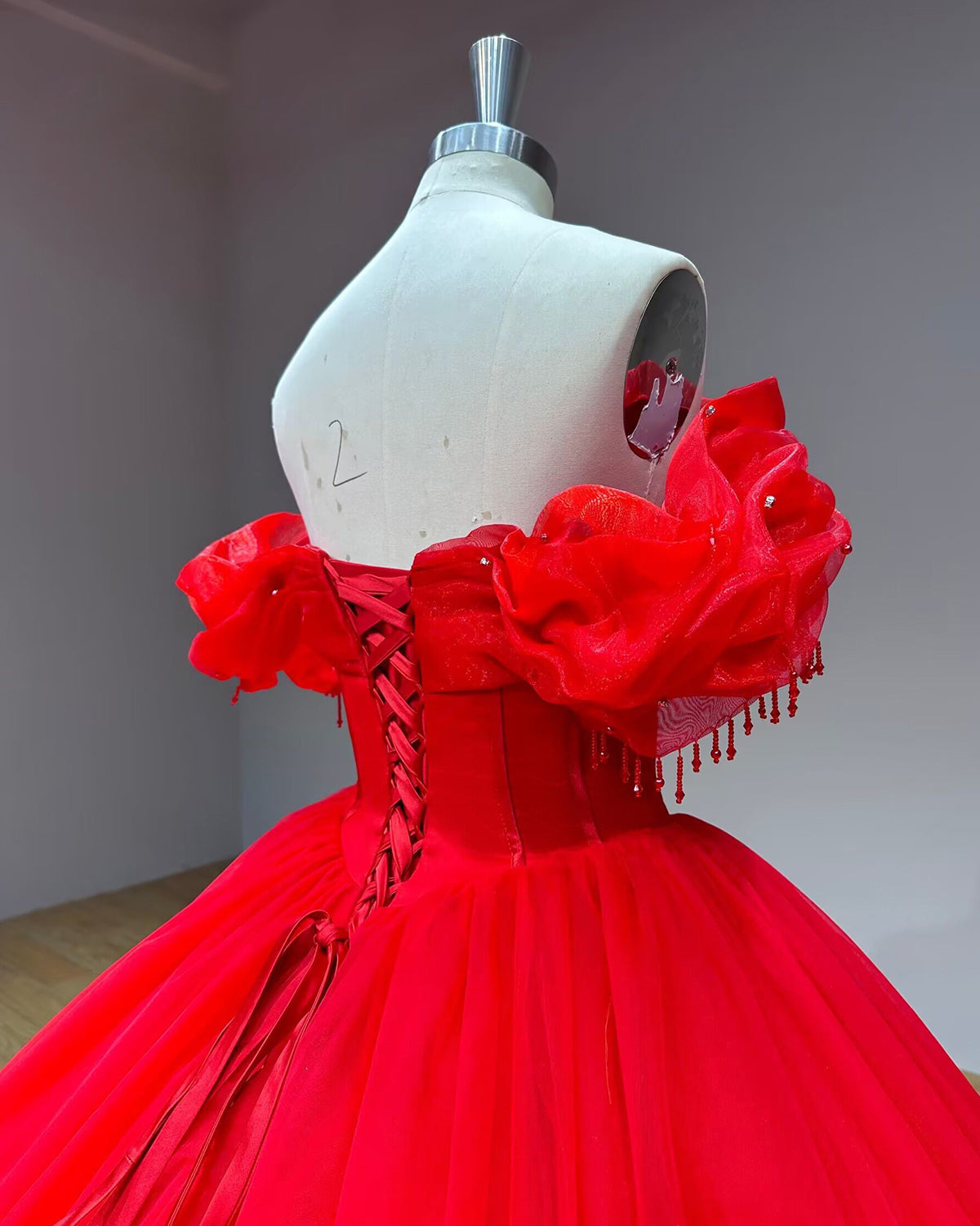 Three-quarter back profile shot of the structured red corset bodice on a mannequin, showcasing the clean lines and pleated off-the-shoulder sleeve detail.