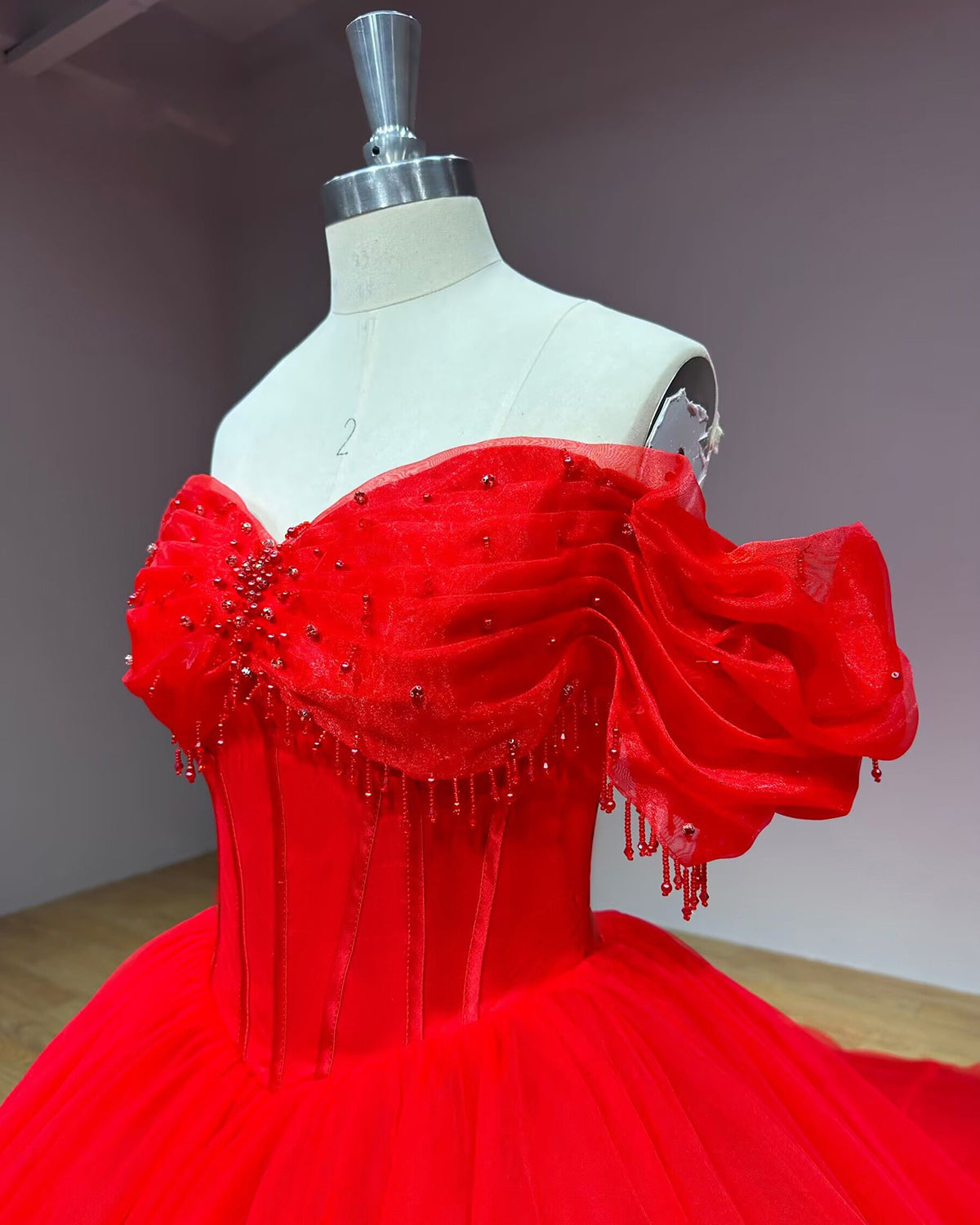 Side front profile detail of the red bridal gown bodice highlighting the sweetheart neckline, clustered crystal beadwork, and off-the-shoulder sleeve drapes.