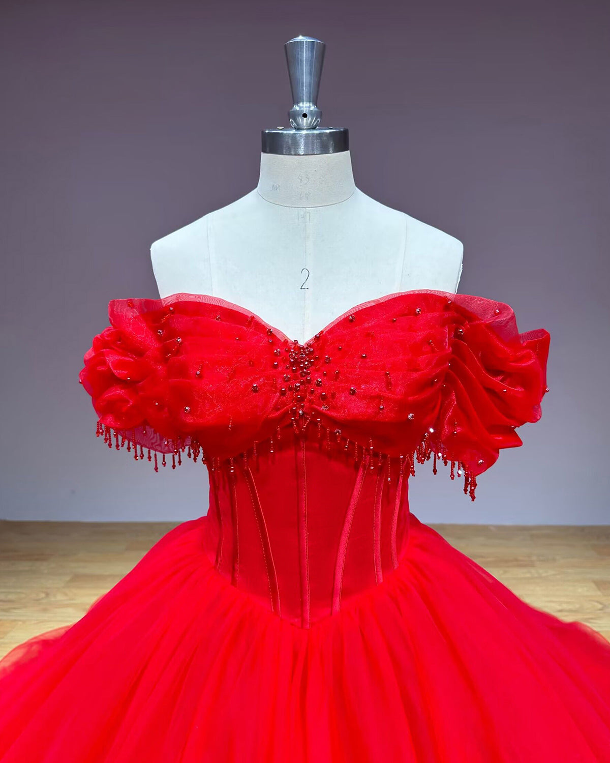 Close-up front view of the red sweetheart neck dress bodice emphasizing the structured corset boning, centered red bead embellishments, and hanging fringe trim.
