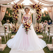 Bride posing in a luxury A-line wedding dress with a colorful floral embroidered bodice under a floral arch at an outdoor wedding ceremony.