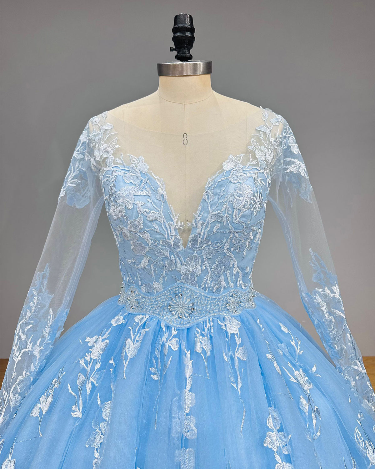 Close-up of a blue bridal gown bodice emphasizing the deep V-neckline, sheer long sleeves, and an intricately beaded silver belt.