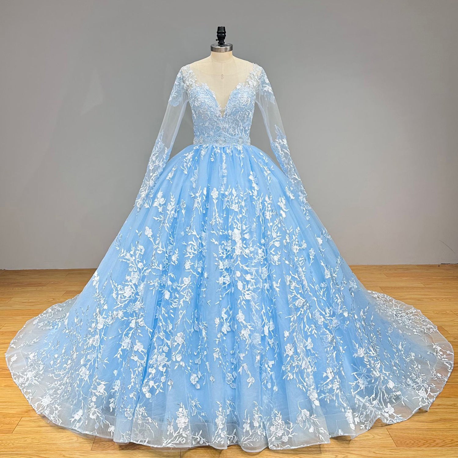 Front view of a pastel blue princess ball gown bridal dress featuring a sheer illusion plunge bodice and a dramatic flared tulle skirt on a dress form.