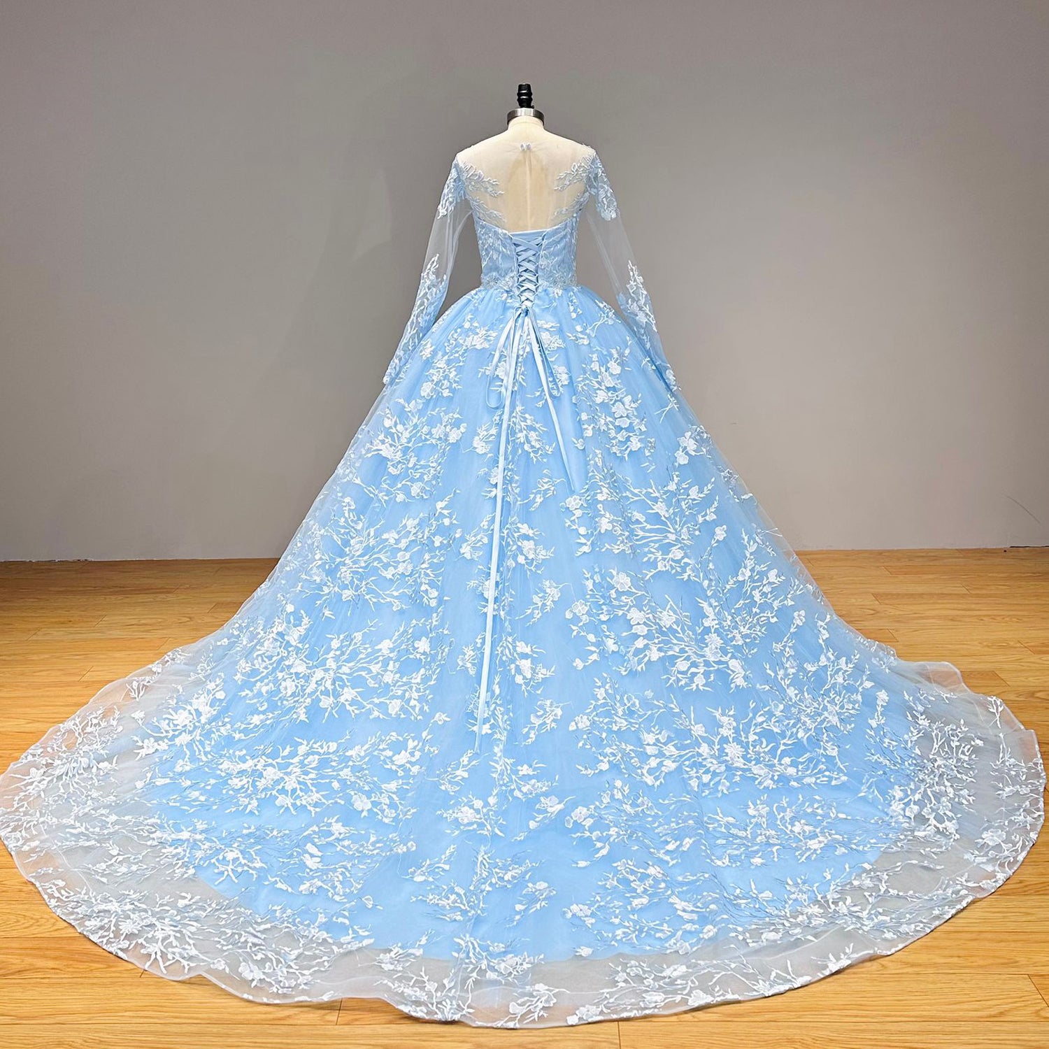 Full back view of a light blue long-sleeve wedding dress highlighting a traditional lace-up corset closure and a wide, sweeping embroidered train.
