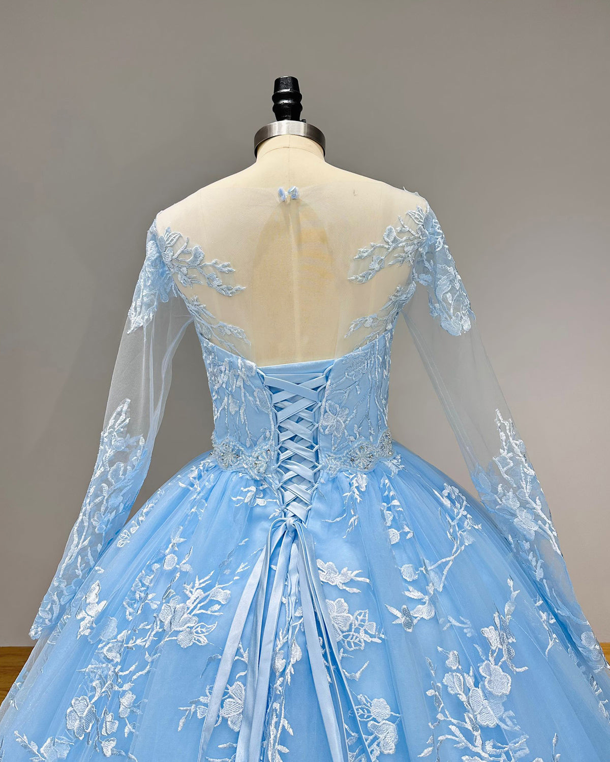 Detailed view of the back of a blue bridal gown showing the adjustable satin ribbon corset back beneath a sheer illusion lace yoke.