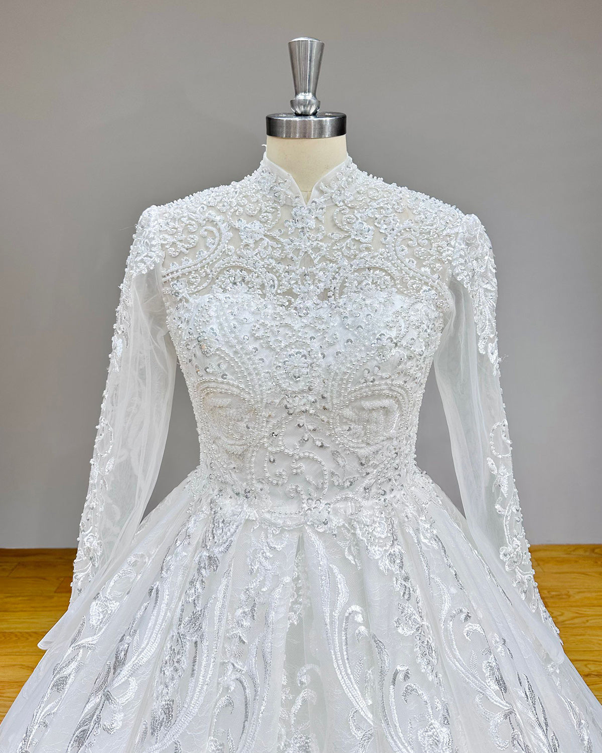 Close-up back bodice detail of a luxury wedding gown on a mannequin, showcasing the sheer high neck with delicate pearl buttons, a classic corset lace-up back, and beaded long sleeves.