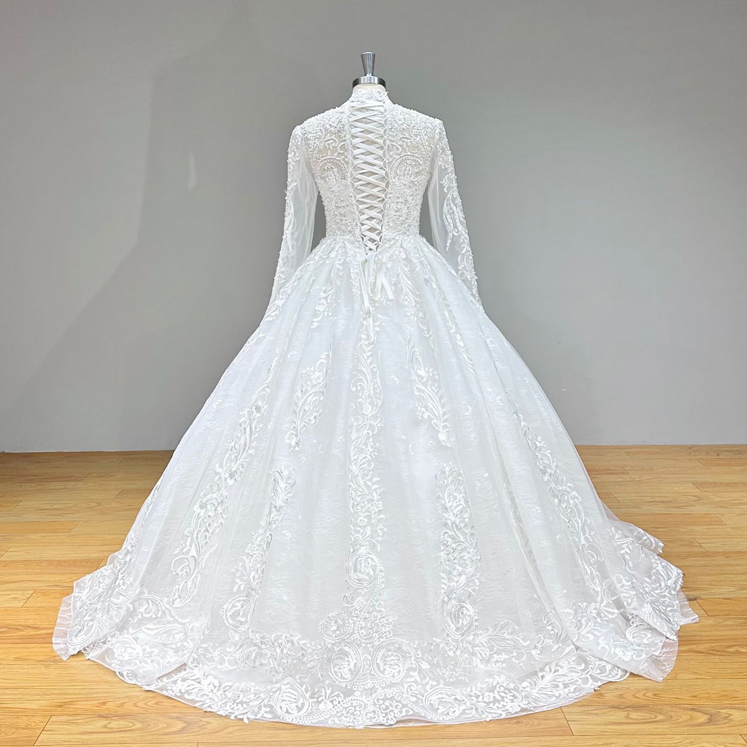 Dramatic full back view of a luxury high neck ball gown wedding dress on a mannequin, displaying the beaded pearl long sleeves, traditional lace-up corset, and a wide, sweeping sparkling train.
